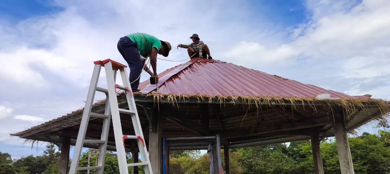 Two workers fastening a new red metal roof onto a gazebo at the Children's Center